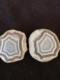 Matched pair of Lebanese banded agate geode halves from Minieh shore, showing crisp octagonal concentric banding in gray, white, and cream.
