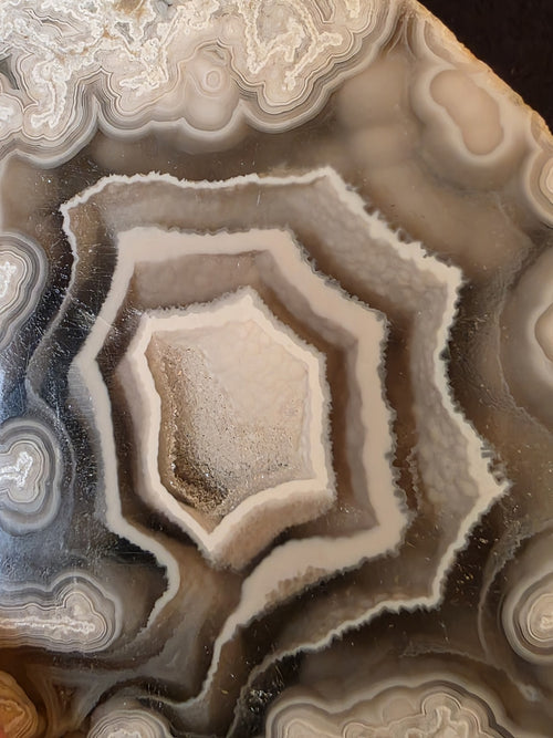 Close-up of the polyhedral chamber formation in Lebanese agate geode №001, showing angular diamond and pentagonal banding in olive-brown and cream.
