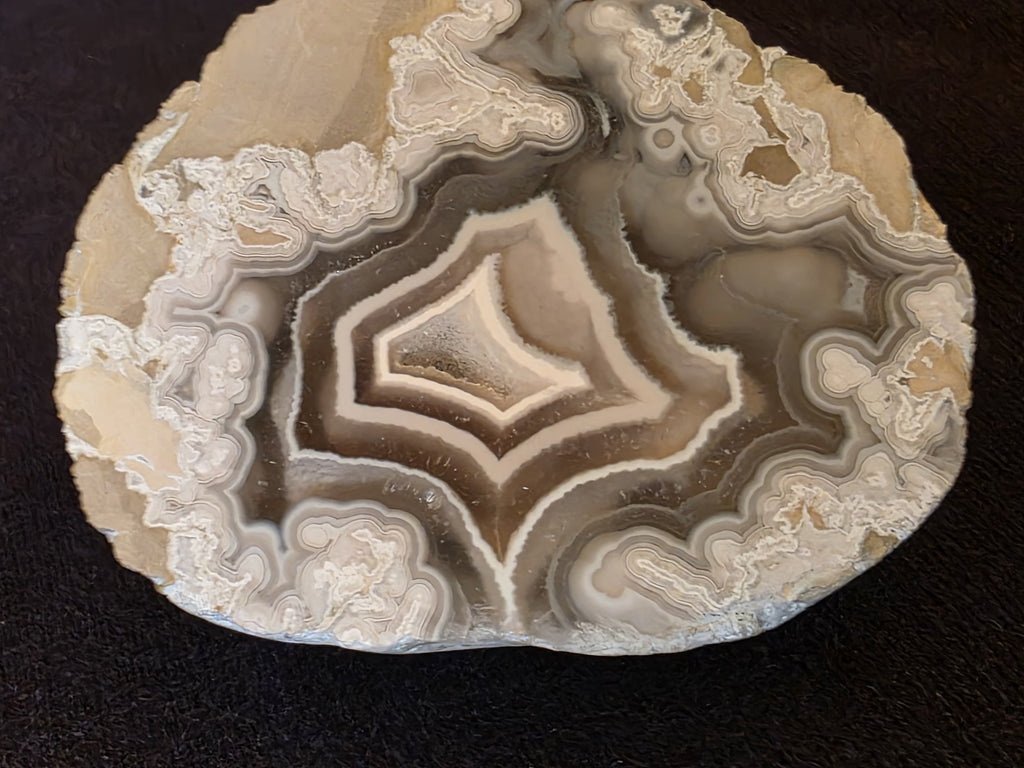 Matched pair of Lebanese polyhedral agate geode halves from Minieh shore, showing mirror-image concentric chambers in cream, olive, and gray tones on dark felt background.
